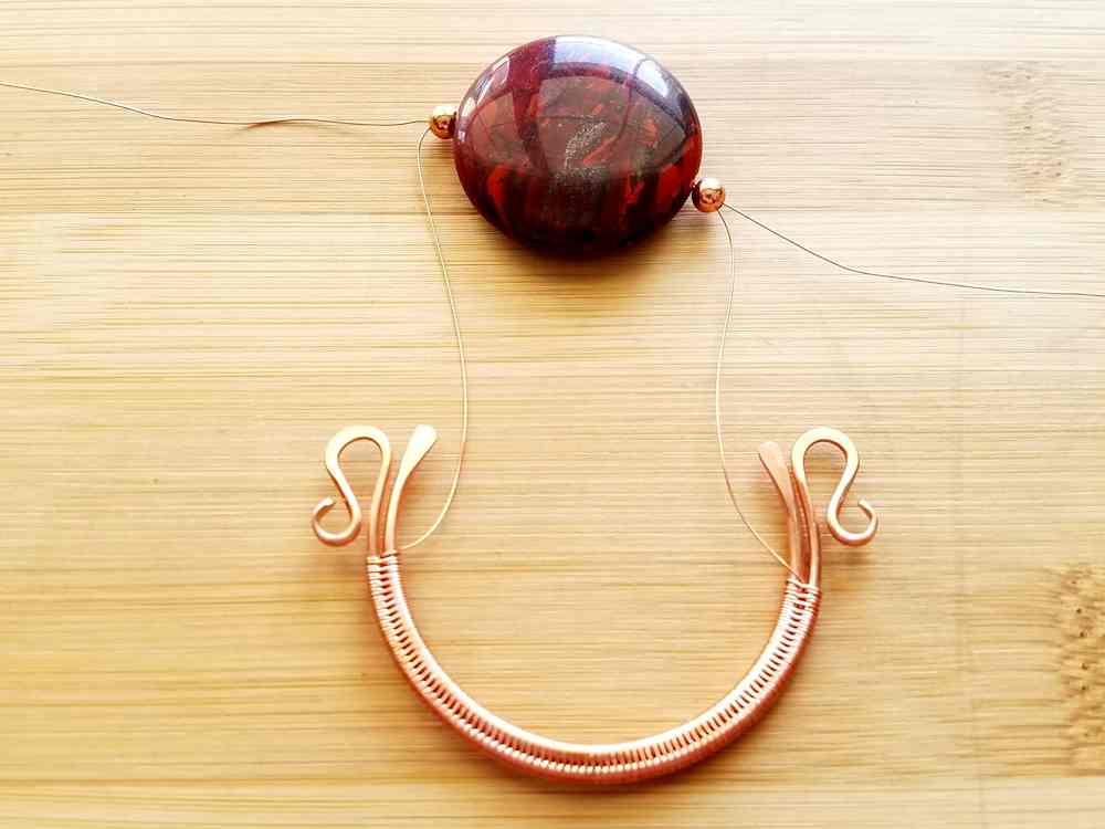 Step 6 - Lay your focal bead on your work surface above the wire frame, as shown, and feed your weaving wires through the spacer beads and focal bead. One from left to right and the other from right to left.