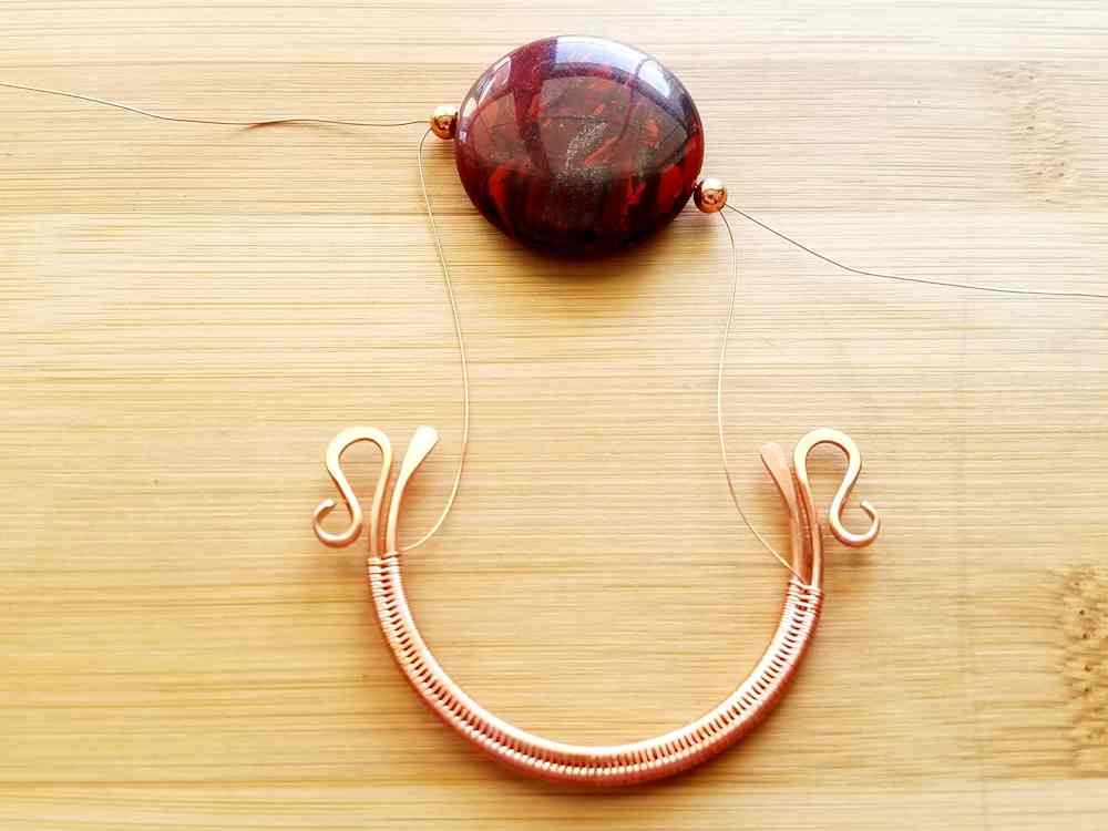 Step 6 - Lay your focal bead on your work surface above the wire frame, as shown, and feed your weaving wires through the spacer beads and focal bead. One from left to right and the other from right to left. 