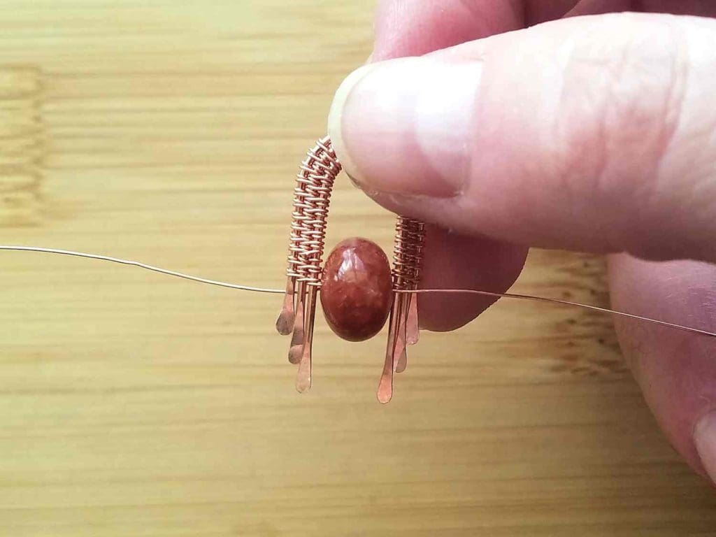 Step 7 - Gently pull the ends of the weaving wires until the bead slides up into position within the woven bead frame, as shown. 