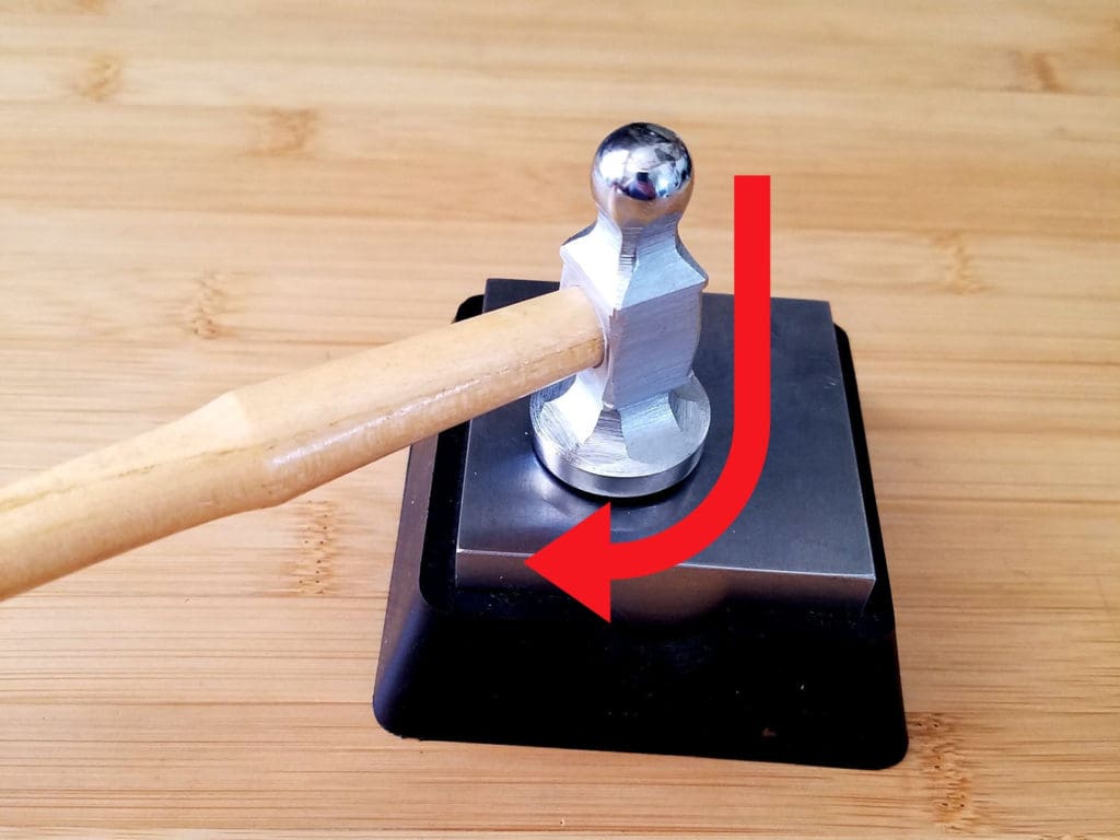The key to drawing your wire out into a specific shape is to pull the head of the hammer back along the length of the wire just as you make contact. The shape of this stroke is something like the letter J as indicated by the arrow in this image.