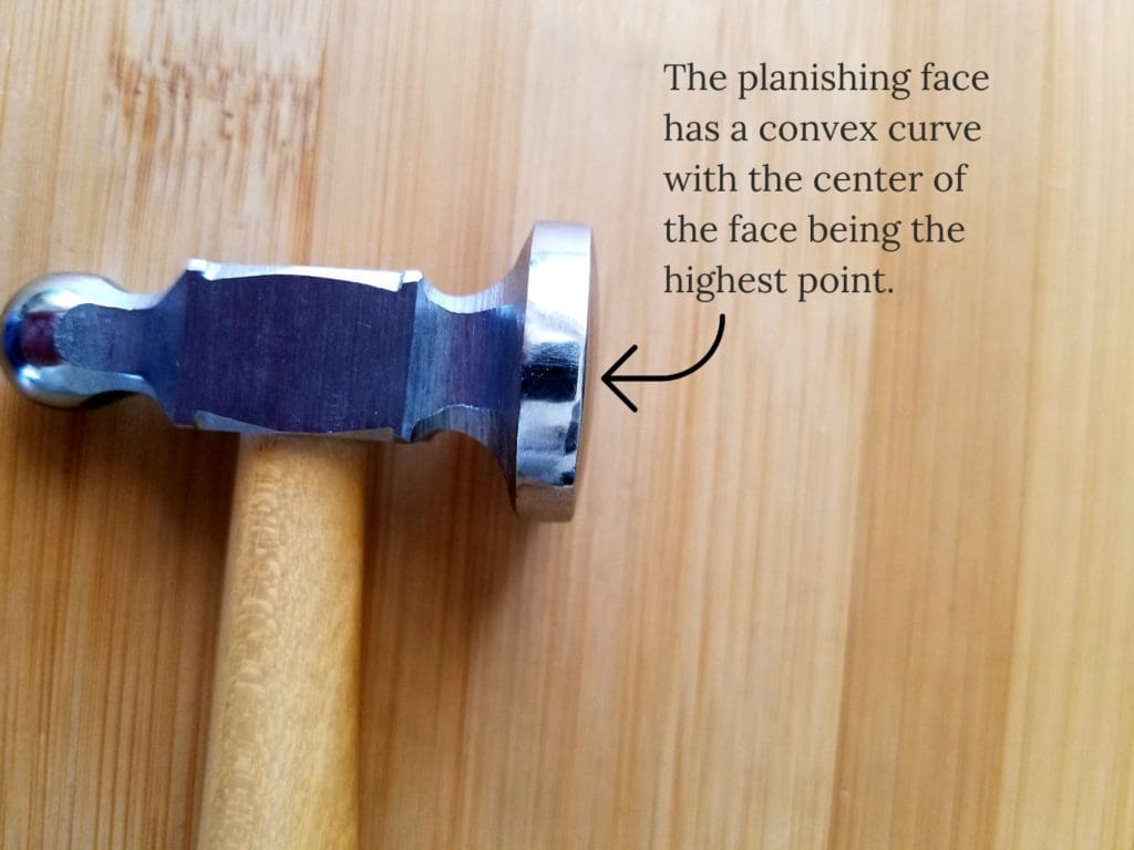 The planishing face of the chasing hammer has a slightly convex surface with the center of the face being the highest point, as shown in this image.