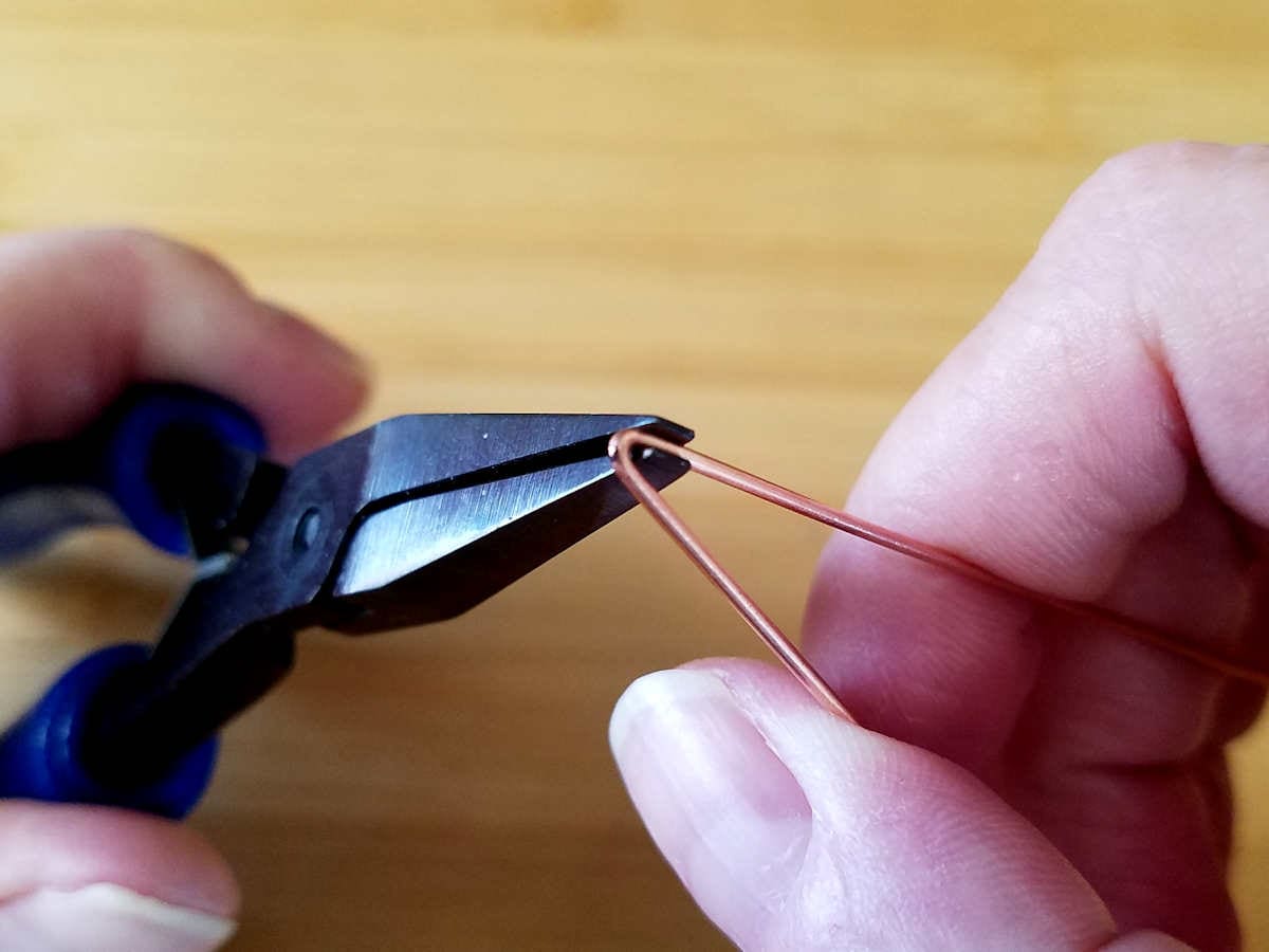 Here the author is using flat nose pliers to fold the 9-inch frame wire in half.