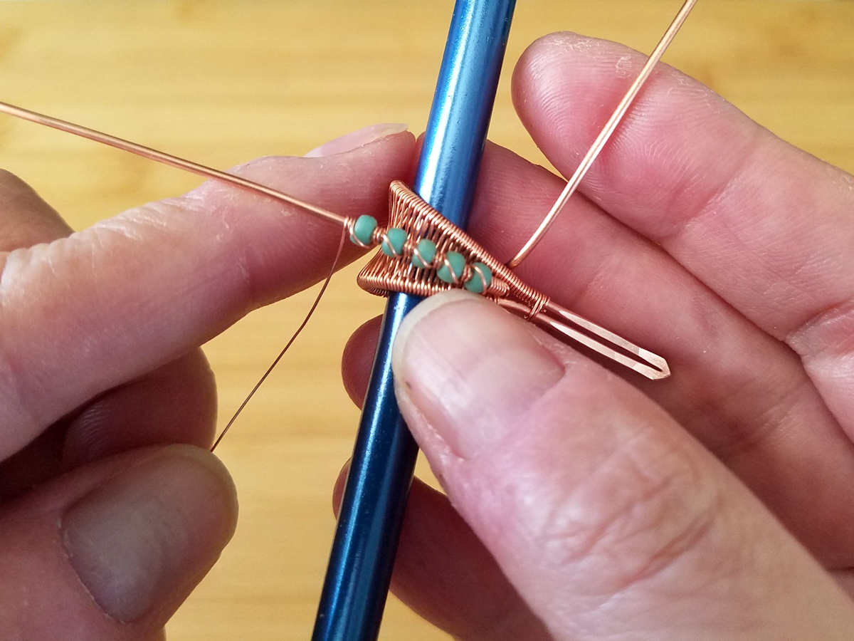In this image, the author is securing the beads by wrapping them with the weaving wire. 