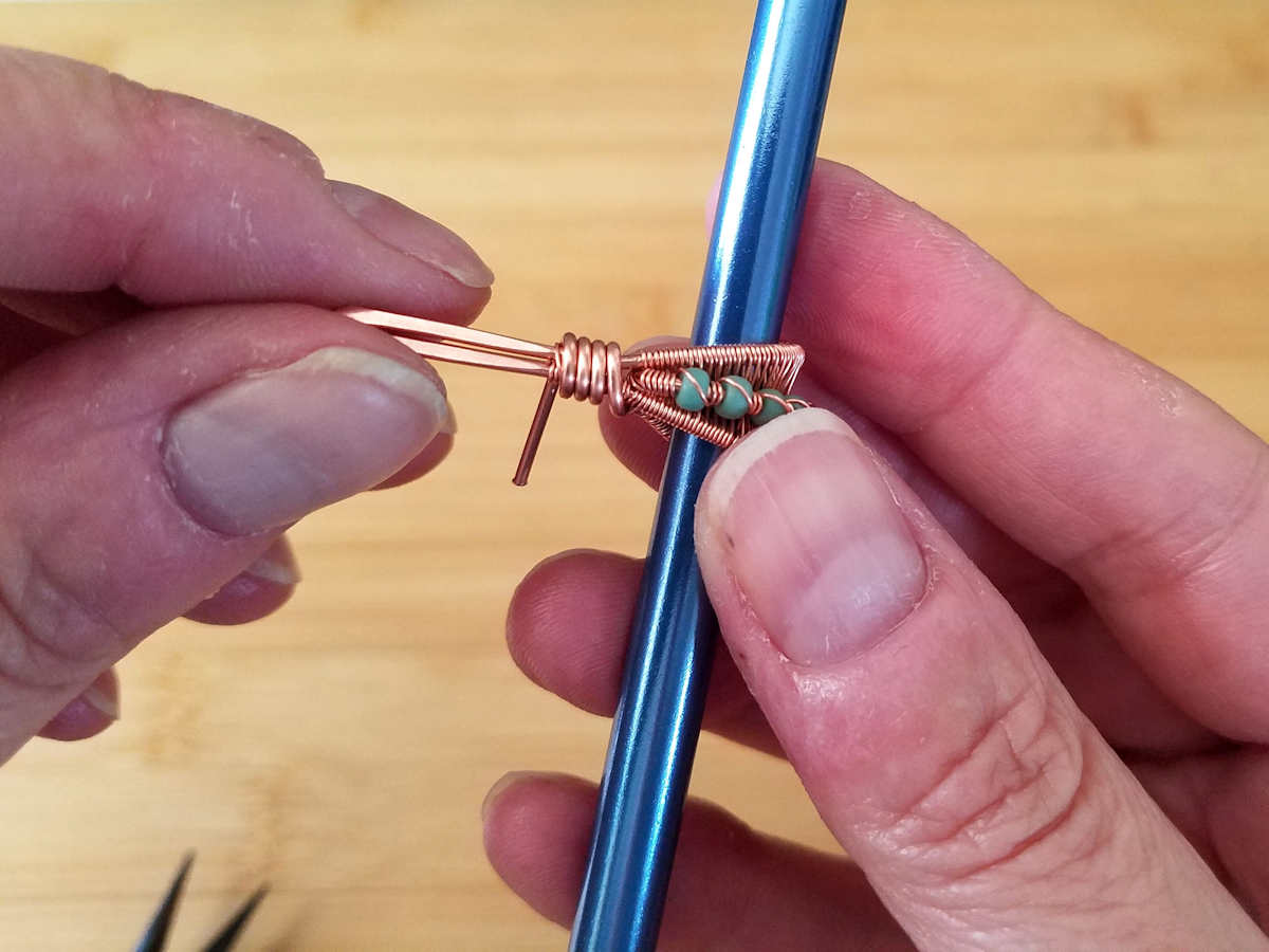 In this image, the author is coiling the remaining core wire around the folded point of the bail and the central core wire. This coil will secure the beaded core in position.