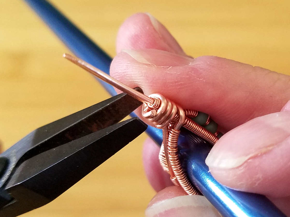 In this image, the author has trimmed the coiled wire and is now tucking the cut end in place against the beaded core wire behind the folded point of the bail. 