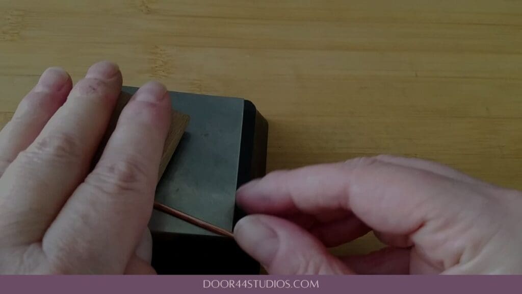 Straightening the wire for the stick pin by pressing and rolling it on the bench block with a hardwood wedge